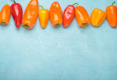 Birkaç renkli taze biber mavi arkaplan üzerinde yatay bir çizgi oluşturarak metin eklemek ve uzayı kopyalamak için kullanılabilecek boş bir alan bırakıyor.