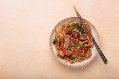 Susam tohumu ve maydanozla süslenmiş bir kase lezzetli udon eriştesi yemek çubukları ve limon dilimleri ile bej bir masada servis ediliyor. Metin için boşluk