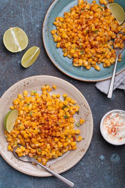 İki tabak esquite, popüler bir Meksika sokak yemeği, limon dilimleri ve acı biberli ekşi krema ile servis edilir.