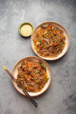 Geleneksel Kore eriştesi, iki kase Japon eriştesi. Renkli sebzeler ve baharatlı etle kızartılmış patates şehriyeli bir yemek.