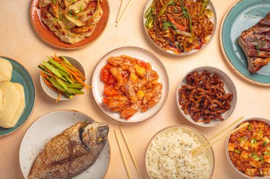 Variety of delicious chinese dishes on plates and bowls arranged on a table: kung pal chicken, sweet and sour pork, noodles, dumplings, mapo tofu, fish, rice top view clipart