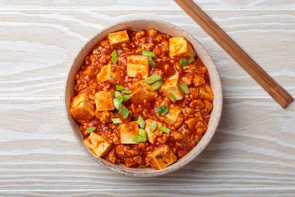 Mapo tofu, popüler bir Çin Sichuan yemeği, bir kasede servis edilir ve yeşil soğanla süslenir, beyaz ahşap arka planda.