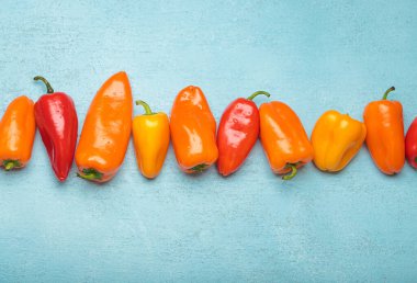 Birkaç renkli taze biber mavi arkaplan üzerinde yatay bir çizgi oluşturarak metin veya diğer grafik elementleri eklemek için kullanılabilecek boş bir boşluk bırakıyor