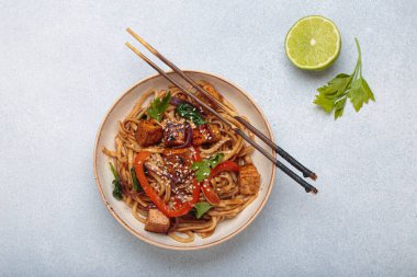 Sebzeli Udon eriştesi ve bir kasede kızarmış tofu yemek için hazır. Tofulu Asya eriştesi, ıspanak, biber, susam tohumu ve mavi ışıklı arka planda çubuklar.