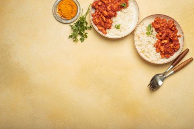 Pirinçli iki tabak körili tavuk, garnitür olarak küçük bir kase zerdeçal ve maydanozla birlikte sarı bir zemin üzerinde yemeye hazır.