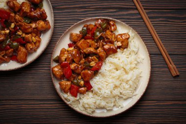 İki tabak Çin kung pao tavuğu, pilav, sebze ve baharatlı soslu fıstık. Ahşap arka planda üst manzara. Öğle veya akşam yemeği için mükemmel.
