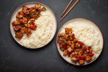 İki tabak Çin kung pao tavuğu, pilav, sebze ve baharatlı soslu fıstık. Koyu arkaplanda üst görünüm. Öğle veya akşam yemeği için mükemmel.