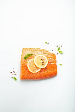 Taze çiğ somon balığı filetosu beyaz arka planda limon, kaba tuz ve yeşil otlarla izole edilmiş. Sağlıklı beslenme ve dengeli beslenme.