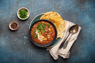 Geleneksel Hint Punjabi yemeği mercimek ve siyah kasede fasulye ile Dal Makhani naan düz ekmek, taze kişniş ve iki kaşık mavi beton kırsal masa manzaralı.