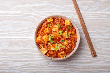 Mapo tofu, popüler bir Çin Sichuan yemeği, bir kasede servis edilir ve yeşil soğanla süslenir, beyaz ahşap arka planda.