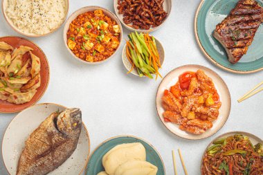 Tabaklardaki lezzetli Çin yemekleri ve tabaklar beyaz bir masaya dizilmiş kung pal tavuğu, tatlı ve ekşi domuz eti, erişte, mantı, mapo tofu, balık, pirinç üstü görünümü. Boşluğu kopyala