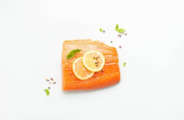 Taze çiğ somon balığı filetosu beyaz arka planda limon, kaba tuz ve yeşil otlarla izole edilmiş. Sağlıklı beslenme ve dengeli beslenme.