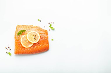 Taze çiğ somon balığı filetosu beyaz arka planda limon, kaba tuz ve yeşil otlarla izole edilmiş. Sağlıklı beslenme ve dengeli diyet. Metin için boşluk.