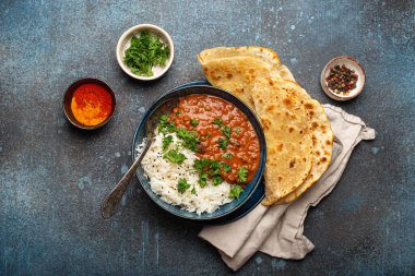 Geleneksel Hint Punjabi yemeği Dal Makhani mercimek ve siyah kasede fasulye bazmati pilavı, naan düz ekmek, taze kişniş ve mavi beton kırsal masa manzaralı kaşık ile servis edilir..