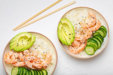 Üzerinde pirinç, karides, avokado, sebze, susam tohumu ve tahta çubuklar olan iki beyaz seramik kâse beyaz beton arka plan manzaralı. Sağlıklı Asya tarzı dürtme kasesi.