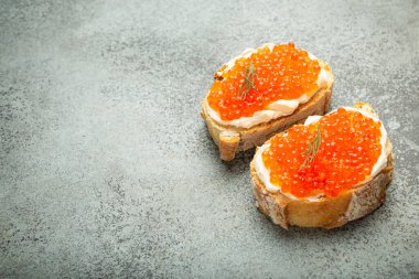 Gri beton arka plan, şenlikli lüks lezzet ve aperatif üzerine tereyağlı ve kırmızı somon havyarlı iki havyar tostu. Metin için boşluk.