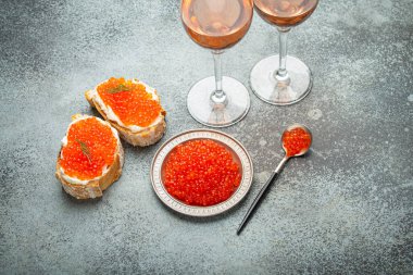 Kırmızı somon havyarlı küçük metal tabak, iki havyar tostu kanepesi, gri beton arka planda iki bardak şampanya, şenlikli lüks lezzet ve aperatif..
