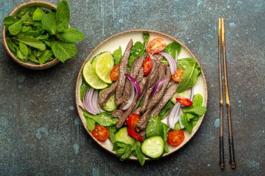Geleneksel Tayland bifteği salatası, sebzeli ve naneli. Beton kaplama arka planda servis ediliyor. Sağlıklı egzotik Asya yemeği..