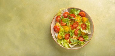 Taze ve canlı karışık salata, kıtır marul, sulu kırmızı ve sarı vişneli domates ve roka. Yanında çatal bıçak takımı olan bir kasede servis edilmiş. Vitaminler ve sağlıklı yeme alışkanlıkları