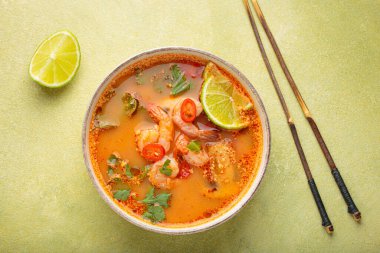 Geleneksel baharatlı Tayland çorbası Tom. İçinde karides, limon, kırmızı biber, kişniş ve yeşil arka planda çubuklar var. Tayland yemeği.