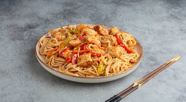 Teriyaki tavuklu waok noodle ve havuç dahil taze sebze, susam tohumlu dolma biber gri dokulu arka planda servis edilir.
