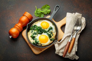 Tahta bir tahtanın üzerinde ıspanaklı iki sahanda yumurta, sağlıklı bir kahvaltı.