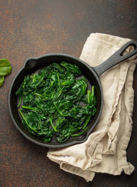 Taze buğulanmış ıspanak yaprakları dökme demir bir tavada, besleyici ve lezzetli bir meze veya sağlıklı yemekler için malzeme olarak servis edilir.