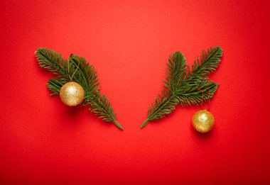 Geyik boynuzu şeklinde zarif bir şekilde düzenlenmiş altın noel baloları, çam kozalakları, köknar dalları ve kırmızı arka planda paketlenmiş bir hediye kutusu, neşeli bir tatil atmosferi yaratıyor.