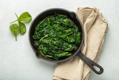 Taze buğulanmış ıspanak yaprakları dökme demir bir tavada servis edilir, bej bir peçetenin üzerinde dinlenirler, sağlıklı beslenirler ve canlı yeşil sebzeler