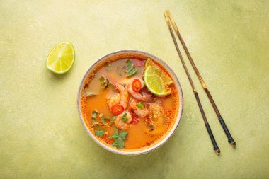 Geleneksel baharatlı Tayland çorbası Tom. İçinde karides, limon, kırmızı biber, kişniş ve yeşil arka planda çubuklar var. Tayland yemeği.