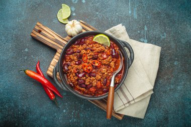 Meksika Chili con Carne, kireç kamaları ve ahşap kesme tahtasına yerleştirilmiş kırmızı biber ve sarımsak ile süslenmiş dökme demir bir tavada servis edilir.