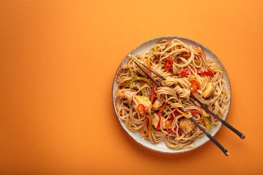 Asya erişteleri tavukla, havuçla, biberle ve kırmızı biberle kızarır. Portakal arka planında yemek çubuklarıyla servis edilen canlı ve lezzetli bir yemek yapar.