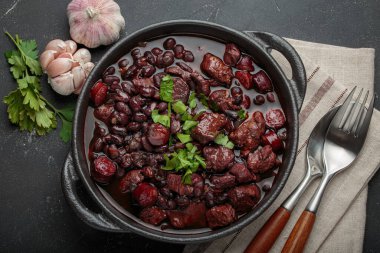 Feijoada, dökme demir bir tencerede geleneksel Brezilya güveci, yanında taze sarımsak ve maydanoz, keten peçetede çatal ve kaşıkla servis edilmeye hazır.