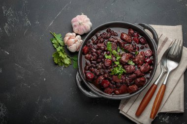 Feijoada, dökme demir bir tencerede geleneksel Brezilya güveci, yanında taze sarımsak ve maydanoz, keten peçetede çatal ve kaşıkla servis edilmeye hazır,