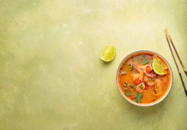 Geleneksel baharatlı Tayland çorbası Tom. İçinde karides, limon, kırmızı biber, kişniş ve yeşil arka planda çubuklar var. Tayland yemeği.