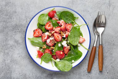 Taze çilekli hafif sağlıklı yaz salatası, ıspanak, krem peynir ve ceviz beyaz seramik tabakta, kırsal gri arka plan Top View.