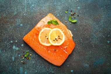 Taze çiğ somon filetosu koyu mavi kırsal beton masa arka planında limon, kaba tuz, yeşil otlar üst manzara. Sağlıklı yemek ve dengeli beslenme.