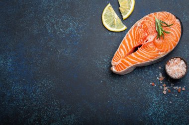 Taze çiğ somon bifteği koyu mavi taştan arka planda, gül tuzu ve limon üst görüşlü, sağlıklı dengeli beslenme ve balıkla beslenme. Metin için boşluk