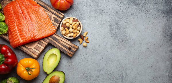 Fresh raw salmon fillet on wooden cutting board, organic bio vegetables and nuts on rustic stone grey background top view. Ingredients full of vitamins for healthy diet and nutrition, space for text