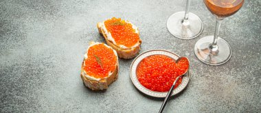 Kırmızı somon havyarlı küçük metal tabak, iki havyar tostu kanepesi, gri beton arka planda iki bardak şampanya, şenlikli lüks lezzet ve aperatif..