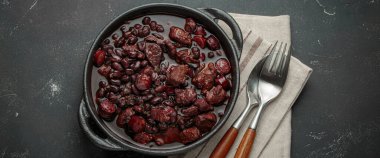 Feijoada, dökme demir bir tencerede geleneksel Brezilya güveci, keten peçetede çatal ve kaşıkla servis edilmeye hazır.