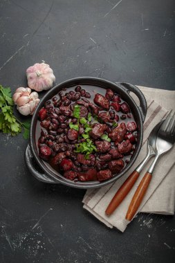Feijoada, dökme demir bir tencerede geleneksel Brezilya güveci, yanında taze sarımsak ve maydanoz, keten peçetede çatal ve kaşıkla servis edilmeye hazır.