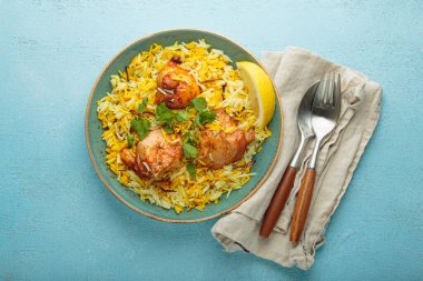 Lezzetli Hintli tavuk biryani tavukla süslenmiş taze kişniş ve limonla süslenmiş mavi bir kırsal masada, yanında çatal bıçak takımı ile. Hindistan 'ın otantik yemeği