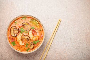 Karides, mantar, limon ve kişniş karışımlı lezzetli Tom çorbası açık bej arka planda yemek çubuklarıyla servis edilir Tayland 'ın lezzetli ve aromatik geleneksel bir yemeğidir.