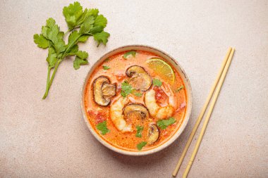 Karides, mantar, limon ve kişniş karışımlı lezzetli Tom çorbası açık bej arka planda yemek çubuklarıyla servis edilir Tayland 'ın aromatik ve geleneksel bir yemeğidir.