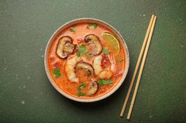 Karides, mantar, limon ve kişniş karışımlı lezzetli Tom çorbası mavi arka planda yemek çubuklarıyla servis edilen Tayland aromalı geleneksel bir yemektir.