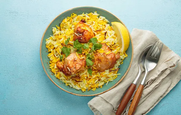Lezzetli Hintli tavuk biryani tavukla süslenmiş taze kişniş ve limonla süslenmiş mavi bir kırsal masada, yanında çatal bıçak takımı ile. Hindistan 'ın otantik yemeği