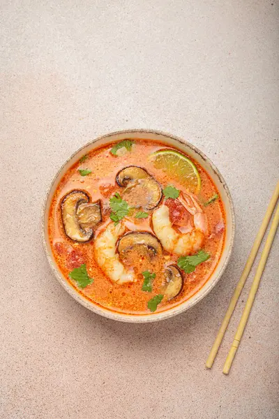 Karides, mantar, limon ve kişniş karışımlı lezzetli Tom çorbası açık bej arka planda yemek çubuklarıyla servis edilir Tayland 'ın aromatik ve geleneksel bir yemeğidir.