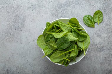 Taze ıspanak yaprakları gri bir arka planda, canlı yeşil renklerini ve sağlıklı cazibelerini sergiliyor, salatalar, meyve suları veya yan yemekler için mükemmel. Boşluğu kopyala