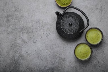 Geleneksel Japon matcha çay seremonisi gri taş arka planda, siyah demir çaydanlık, iki fincan köpüklü yeşil çay ve bir kasede ve kaşıkta kibrit tozu, yazı için yer